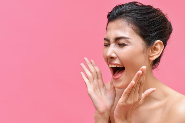 Primer plano de una mujer adulta gritando con los ojos cerrados sobre un fondo rosado