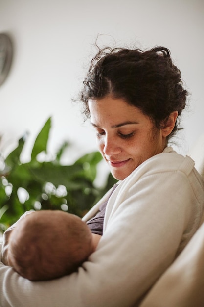 Foto primer plano de una mujer adulta sonriente amamantando a una niña recién nacida en casa