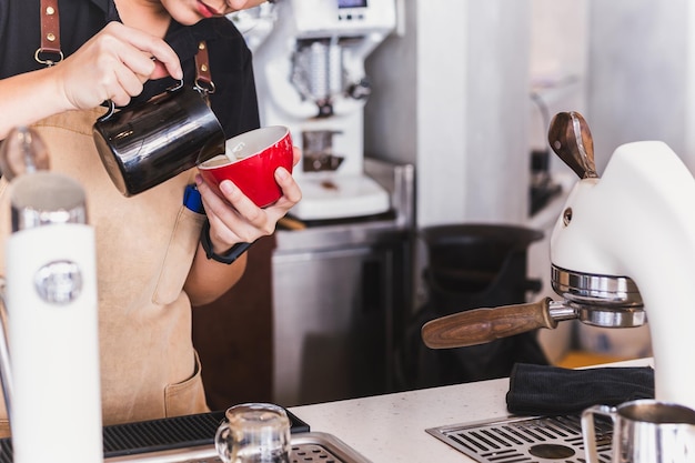 Primer plano de mujer asiática barista haciendo capuchino haciendo arte latte en taza