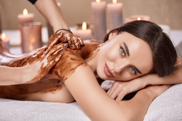 Primer plano de una mujer bonita en spa y con masaje con chocolate en la espalda