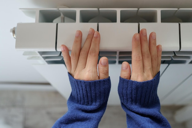 Primer plano de una mujer calentándose las manos en el calentador en casa durante los fríos días de invierno Temporada de calefacción