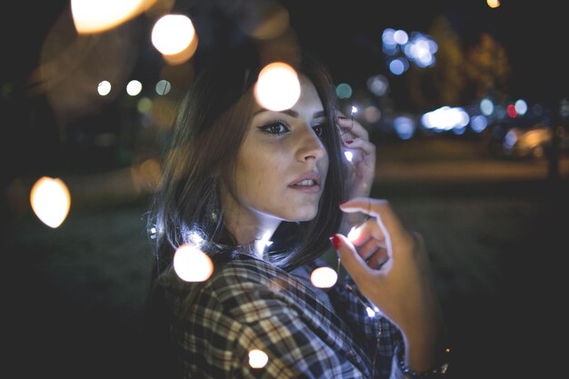 Un primer plano de una mujer caucásica morena con un corte de pelo corto mirando las luces de la ciudad.