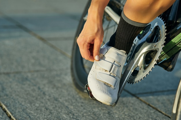 Primer plano de mujer ciclista vistiendo zapatos de ciclismo de sujeción mientras se monta en bicicleta al aire libre