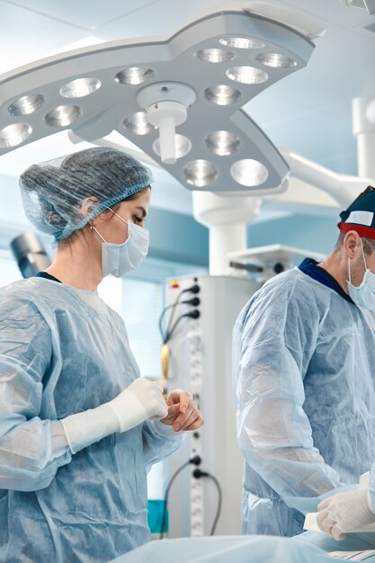 Primer plano de la mujer cirujano, en la mesa de la sala de operaciones con un equipo de colegas que se preparan para la operación Salvar vidas, cirugía moderna.