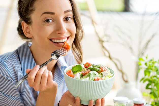 Primer plano de una mujer comiendo ensalada saludable con tomates cherry en interiores