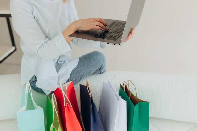 Primer plano de una mujer comprando en línea usando una computadora portátil con coloridas bolsas de compras