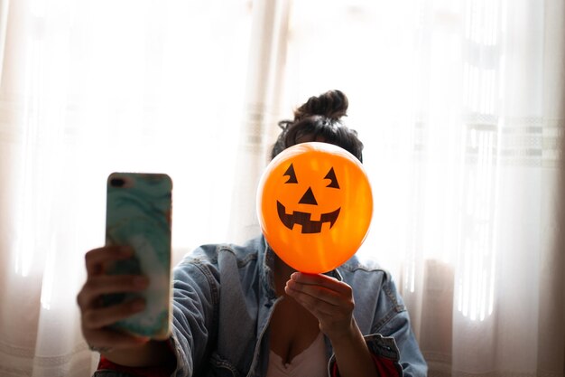 Foto primer plano de una mujer con la decoración de halloween contra la cara y tomando una selfie en casa
