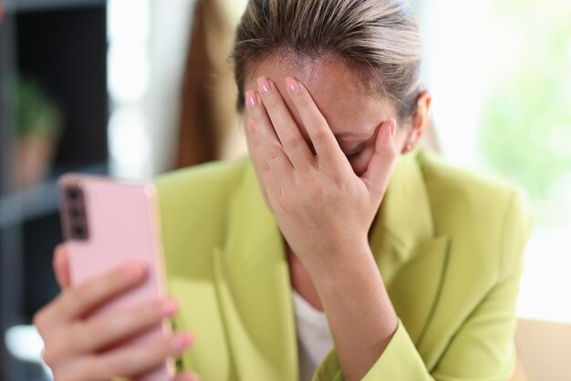 Primer plano de una mujer deprimida frustrada que cubre la cara con la mano femenina sosteniendo el teléfono inteligente y