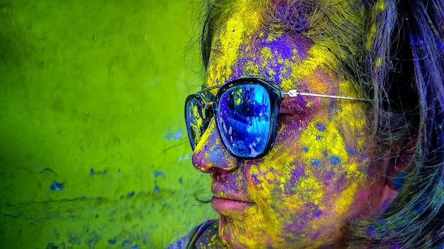 Foto primer plano de una mujer desordenada con pintura en polvo en la cara usando gafas de sol durante holi