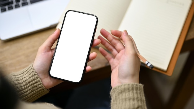 Primer plano de una mujer desplazándose en su teléfono en la maqueta de pantalla blanca de su teléfono de escritorio