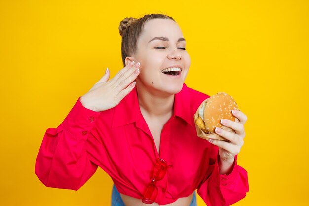 Primer plano de una mujer embarazada con una camisa rosa brillante y comida chatarra Hamburguesa y embarazo El concepto de una mujer embarazada comiendo alimentos poco saludables Una mujer embarazada alegre come comida rápida