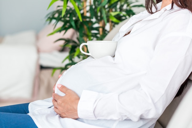 Primer plano de mujer embarazada relajante, sentado en el sofá y tomando té en casa