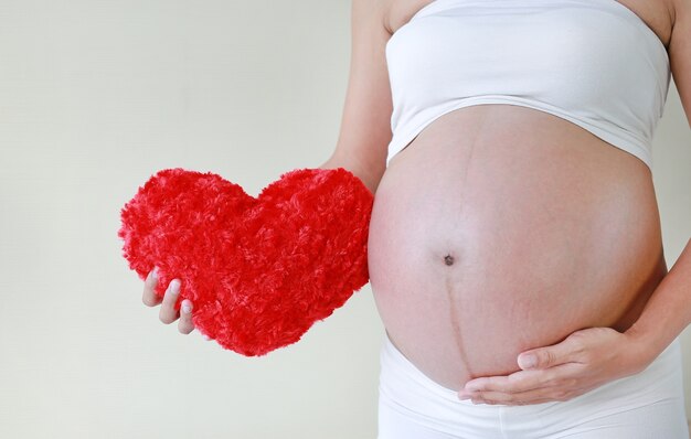 Primer plano Mujer embarazada sosteniendo una almohada corazón rojo en su barriga.