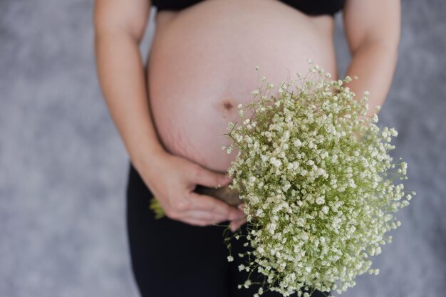 Un primer plano de una mujer embarazada sosteniendo flores en casa.