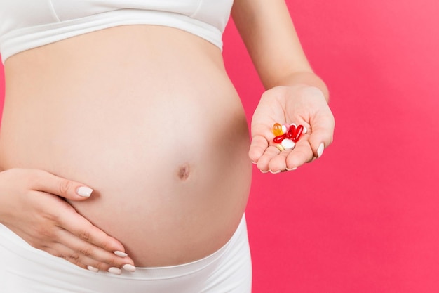 Primer plano de una mujer embarazada sosteniendo un montón de pastillas en un fondo colorido con espacio para copiar Tomando medicamentos y vitaminas durante el concepto de embarazo