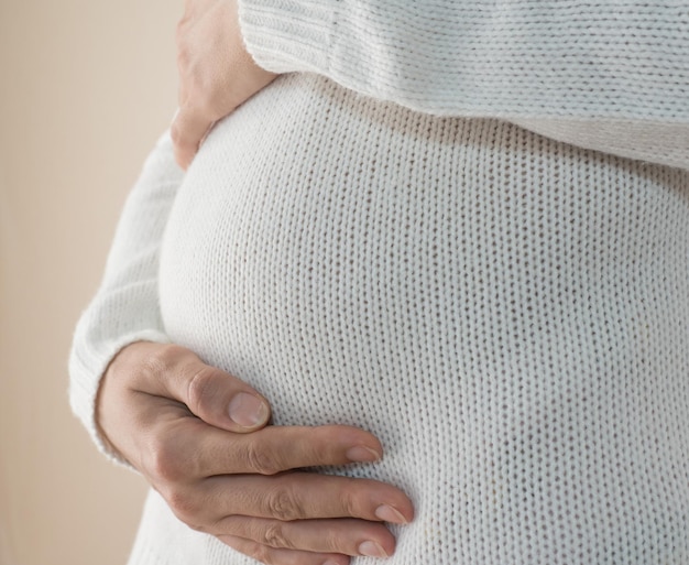 Primer plano de una mujer embarazada en un suéter blanco acariciando su vientre embarazado