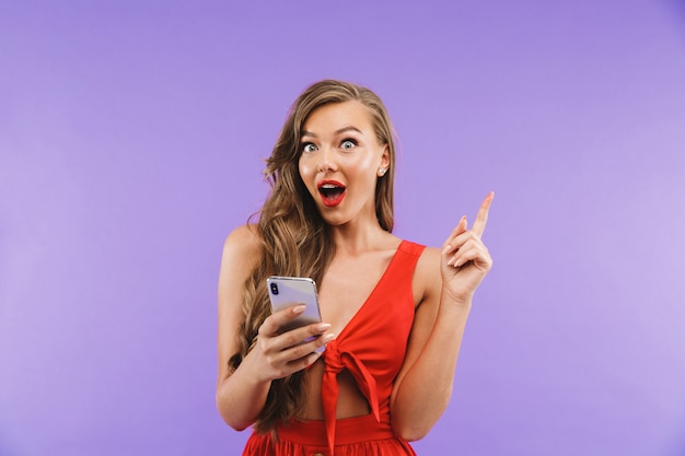 Primer plano de mujer emocionada alegre con vestido rojo sonriendo y sosteniendo teléfono móvil