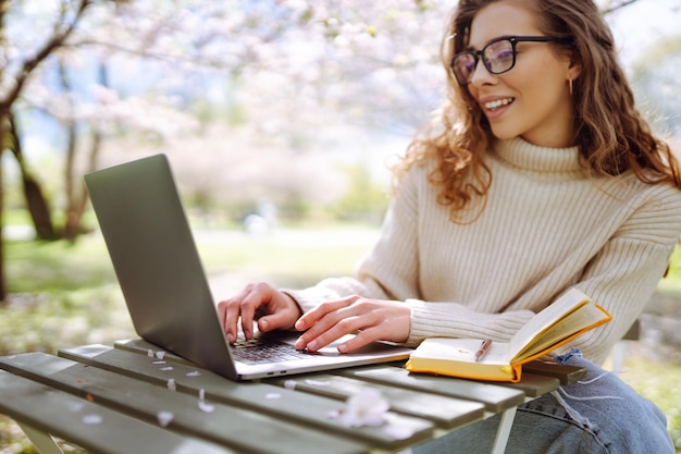 Foto primer plano de una mujer escribiendo a mano en una computadora portátil con un bloc de notas en una mesa en un parque concepto de trabajo remoto