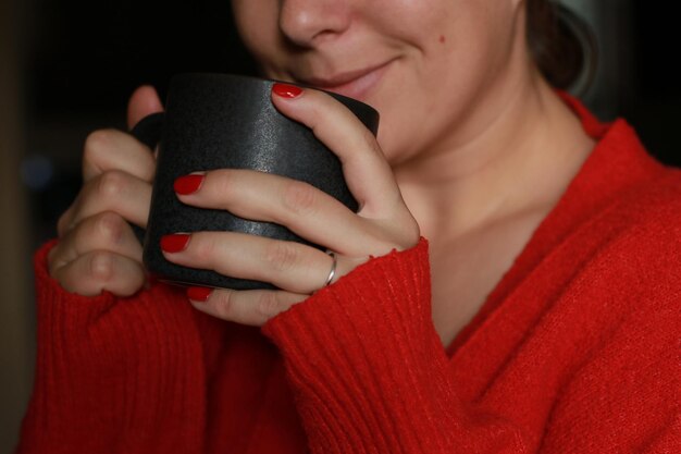 primer plano de una mujer feliz sosteniendo una taza de café gris, usando un suéter rojo cálido y acogedor
