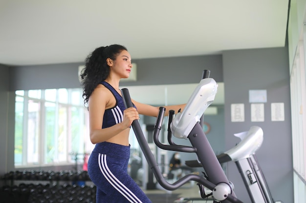 Primer plano de una mujer haciendo ejercicio en una máquina elíptica en el gimnasio