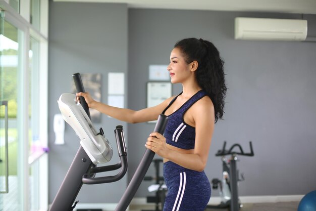 Primer plano de una mujer haciendo ejercicio en una máquina elíptica en el gimnasio