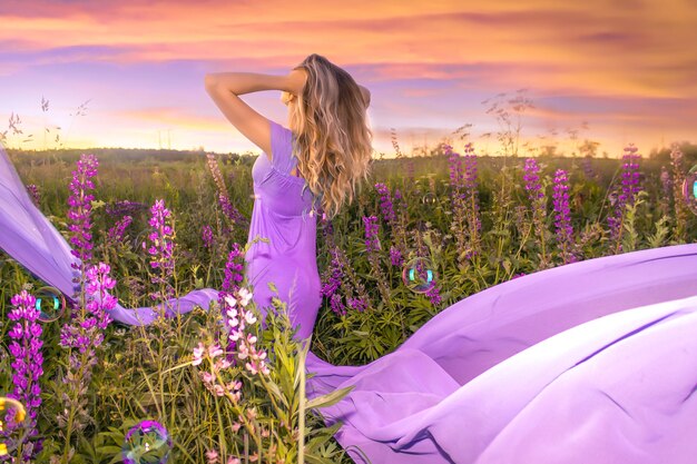 Foto primer plano de la mujer hermosa joven en vestido largo púrpura en el fondo del campo de lupino