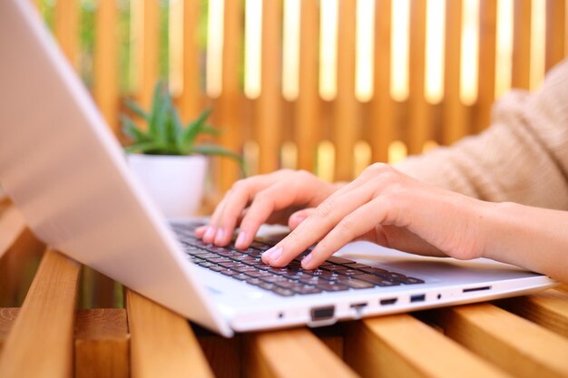 Primer plano de una mujer irreconocible escribiendo en el teclado de una computadora portátil mientras trabaja en un trabajo remoto al aire libre