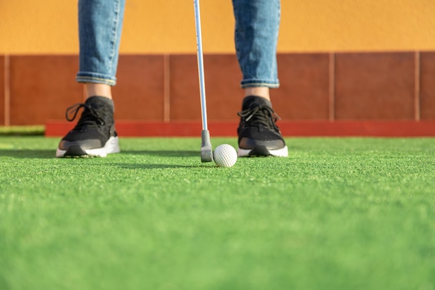 Primer plano de mujer irreconocible golpeando pelota con palo de golf en mini golf