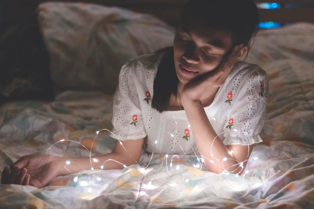 Primer plano de una mujer joven acostada junto a luces iluminadas en la cama