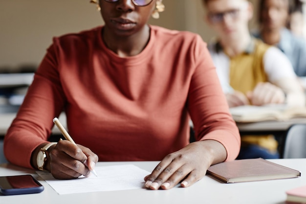 Primer plano mujer joven afroamericana tomando notas mientras estudia en el escritorio en el aula universitaria