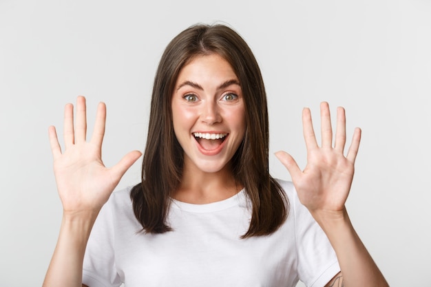 Primer plano de mujer joven atractiva alegre sonriendo, mostrando diez dedos, blancos.