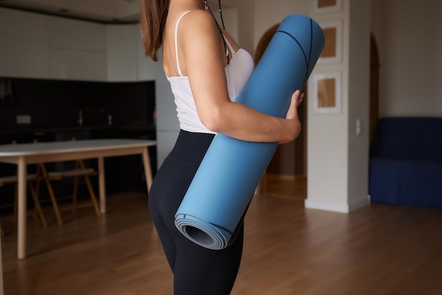 Primer plano de una mujer joven y atractiva que presenta una colchoneta azul de yoga o fitness antes de hacer ejercicio en el estudio Estilo de vida saludable