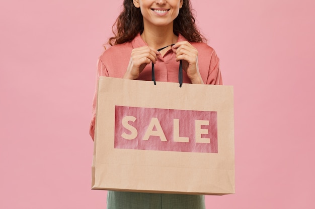 Primer plano de mujer joven con bolsa de papel de gran venta en sus manos aisladas sobre fondo rosa