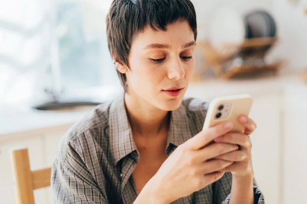 Primer plano de una mujer joven con un corte de pelo corto está usando un teléfono móvil para navegar por las redes sociales