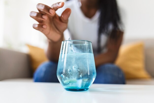 Primer plano de una mujer joven dejando caer un antiácido efervescente en un vaso de agua. mujer joven apenas pone una pastilla soluble con un medicamento para el dolor o la resaca en un vaso de agua