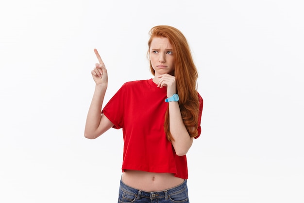 Primer plano de mujer joven estricta estricta viste camisa roja se ve estresado y apuntando hacia arriba con el dedo aislado sobre fondo blanco