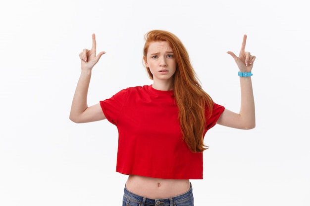 Primer plano de mujer joven estricta y seria viste camisa roja se ve estresado y apuntando hacia arriba con el dedo aislado en blanco