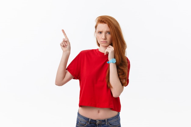 Primer plano de mujer joven estricta y seria viste camisa roja se ve estresado y apuntando hacia arriba con el dedo aislado en blanco