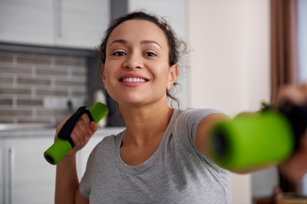 Primer plano de una mujer joven feliz haciendo ejercicio con pesas en casa. Permanecer en el concepto de casa.