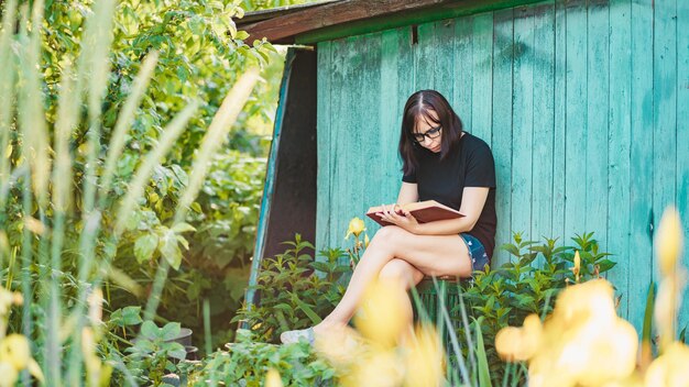 Primer plano de una mujer joven con gafas leyendo un libro en el jardín Mujer descansando en la naturaleza disfrutando de su tiempo libre