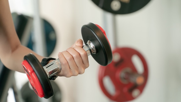 Primer plano de una mujer joven haciendo ejercicio con pesas en el gimnasio.