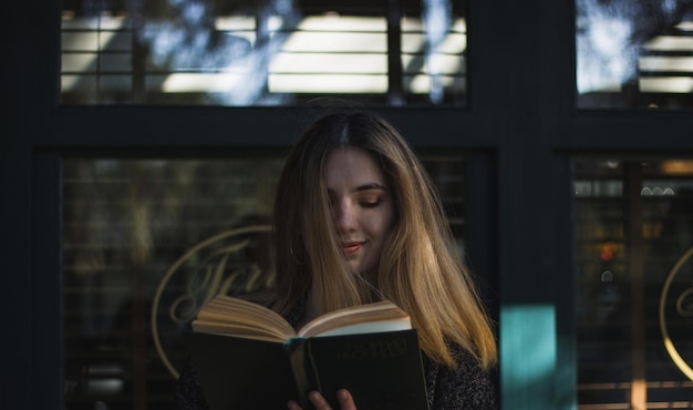 Primer plano de una mujer joven leyendo un libro contra una estructura construida