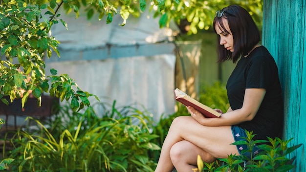 Primer plano de mujer joven leyendo un libro en el jardín Mujer descansando en la naturaleza disfrutando de su tiempo libre