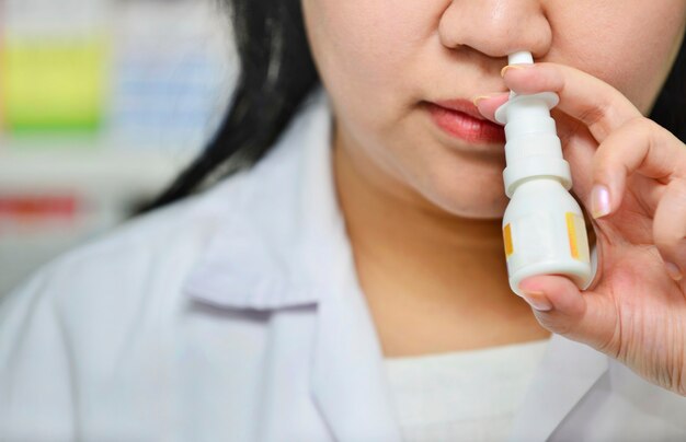 Primer plano de una mujer joven con medicina en aerosol nasal en la farmacia. Problemas de salud estacionales