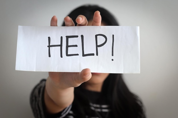 Un primer plano de una mujer joven mostrando un papel con escrito HELP Stop Human Trafficking