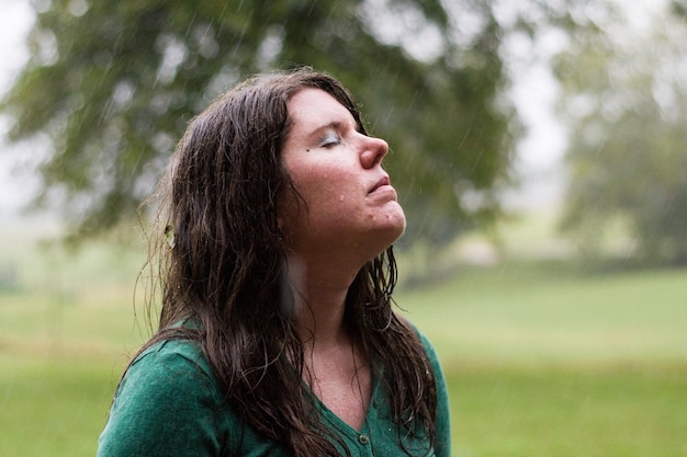 Foto primer plano de una mujer joven con los ojos cerrados de pie en el campo durante un día de lluvia