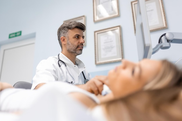 Primer plano de una mujer joven que le examina el cuello con un médico usando un escáner de ultrasonido en una clínica moderna