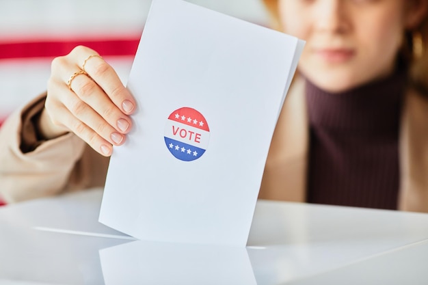 Primer plano de una mujer joven que pone la boleta en la papelera de votación contra el espacio de copia de fondo de la bandera americana