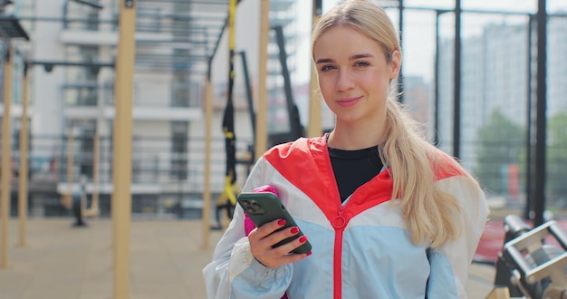 Primer plano de una mujer joven que usa un teléfono inteligente que verifica las aplicaciones de fitness de pie en el campo deportivo Concepto de estilo de vida saludable