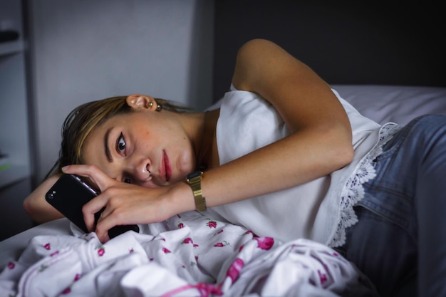 Foto primer plano de una mujer joven usando el teléfono en la cama en casa